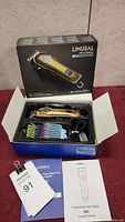 Opened box with Limural hair clippers, colorful attachment combs, charging cord, and user manuals displayed inside box.