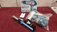 Revlon hair dryer with box and Babyliss Pro curling iron on red surface