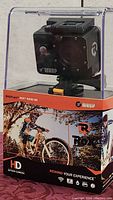 Wasp Cam Rox 9940 HD action camera in clear protective display casing on branded box with outdoor bicyclist image and HD logo.