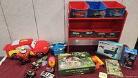 Photo showing the Cars-themed fabric storage organizer and various toys including plush Lightning McQueen, small vehicles, Iron Man mask, dinosaur puzzle, and Nerf blaster.