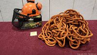 Full view of the orange helmet on box next to coiled rope on red cloth background.