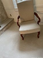 Front view of a formal living room chair showing ivory white and gold fabric upholstery and cherrywood finished curved arms and cabriole legs.