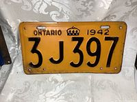 Photo of the full front face of the original 1942 Ontario license plate showing the yellow background with black embossed characters and crown symbol.