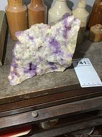 Front and side view of irregular shaped natural amethyst rock with purple crystals and beige-white matrix on wooden surface.