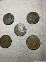 Five circulated US Indian Head pennies arranged with visible obverse Indian Head profile and dates 1884, 1900, 1905, 1908, 1898.