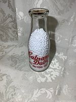 Full view of the vintage Calnans Dairy pint glass bottle filled with white display pellets, showing overall shape and lettering.