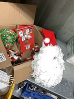 Box opened containing a yarn Santa wall hanging, green stocking with candy cane print, Christmas cards, and several small ornaments including a nutcracker and Christmas figure.