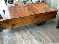 Front angled view of plank wood top and supporting wooden frame with cast iron wheel visible