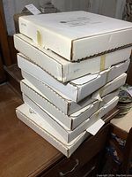 Stack of seven white cardboard boxes for collector plates on a wooden surface