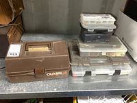 Closed Old Pal 10 50 brown plastic fishing tackle box next to six stacked plastic organizers containing fishing lures and tackle.