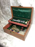 Open jewelry box showing green velvet interior filled with assorted jewelry including three wristwatches on tray and various necklaces, bracelets, and rings below.