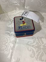 Square Disney tin case showing colorful Mickey Mouse design on lid and "75 Years with Mickey" text.