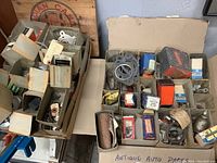 Boxes filled with assorted vintage and antique car and truck parts displayed in original cardboard compartments and packaging.