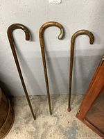 Three wooden canes standing upright against a wall showing different wood finishes and handle shapes.