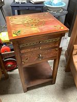 Front and top view of wooden games table with colorful painted floral design on top and drawer fronts.