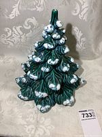 Front view of green ceramic Christmas tree displaying white snow accents and holes for lights.