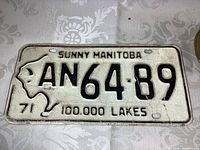 Front side of vintage Manitoba license plate from 1971 showing embossed black text on white background, plate number AN 64 89 with Manitoba map graphic.