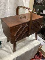 Side view of closed wooden fold-out sewing stand showing dark finish and angled expandable compartments.