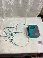 Sony Walkman Sports cassette player with attached matching aqua wired headphones on a white patterned cloth.