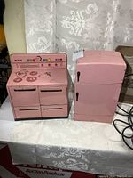 Full overview showing the pink metal toy fridge and matching stove placed side by side on a table.