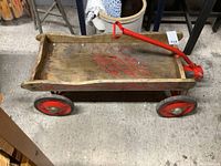 Front angle side view showing wooden box body with visible red graphics and red steel wheels.