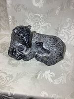Front and side views of the black and gray wolf sculpture curled with pups, showing detailed texture and the chip on toe.