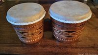 Handmade wooden bongos with leather drumheads shown fully from above with carved pattern visible.