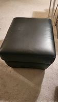 Front view of black upholstered corner ottoman showing smooth surface