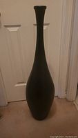Black ceramic vase with tall narrow neck and wide base against a white door background.