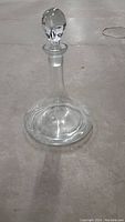 Full view of the vintage clear glass decanter with stopper placed on the floor, showing its shape and size.
