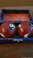 Pair of red exercise balls with yin-yang symbols inside an open decorative box with pink interior.