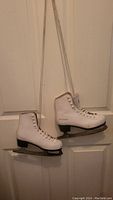 Pair of white junior girls figure skates hanging by their laces showing side and front view.