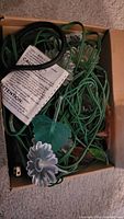 Open box with contents showing green wiring, translucent flower-shaped covers, and leaf details on the string lights.