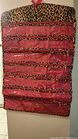 Front view of the pink and leopard print double-sided jewelry holder hanging on a wall, showing rows of clear zipper compartments.