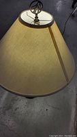 Close-up of the beige fabric lamp shade with brown trim, showing the finial and top details.