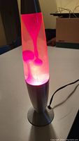Red lava lamp lit and heating showing red wax blobs forming inside clear liquid. Silver metallic base and top.