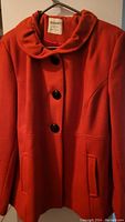Front view of bright red jacket on hanger showing button closure and pocket details