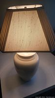 White ceramic lamp base with white fabric shade, lit to show texture and light diffusion.