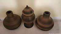 Three brown wicker vases arranged on carpet showing the entire set including the lidded vase in the center and two open vases flanking.