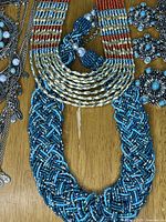 Close-up of the multi-strand and braided beaded necklaces with orange, cream, and blue tones.