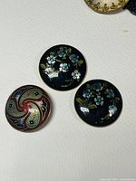 Close-up photo showing three round black enamel buttons with blue floral and bird designs and one ornamental swirl design button.