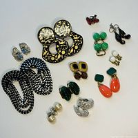 Top view of all 12 pairs of clip on earrings in various styles and colors arranged on white background.