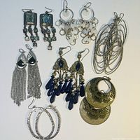Full set of 8 pairs of costume jewelry earrings displayed against a white background. Includes a variety of styles such as hoops, chandeliers, and dangles with different metal tones and decorative details.