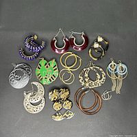 Top-down photo of 11 pairs of assorted costume earrings arranged on a black background. Various colors and styles including hoop and drop designs.