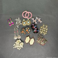 Overview of assorted earrings in hanging and post styles, showing diverse designs and colors including pink, silver, gold, turquoise, black, and white, with some damage and missing stones.