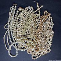 Photo showing a pile of various strands of fake pearl necklaces in ivory and rose gold colors with different bead sizes and a few large prominent pearls.