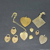 Photo of multiple gold-tone pendants including heart shapes and lock designs on black background.