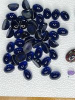 Close-up of dark blue oval cabochon stones, showing glossy surface and some flat backs.