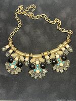 Gold-tone chain necklace with multicolored stones photographed on a black background.