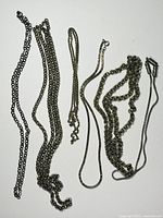 Pile of 6 assorted silver tone chains with varying link styles and lengths placed on white background